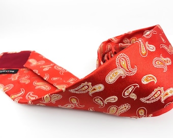 May include: A red paisley patterned silk tie with a burgundy lining. The tie is folded and lying on a white surface.