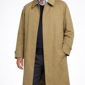 Op de afbeelding: Een beige trenchcoat met een klassiek ontwerp. De jas heeft een kraag, manchetten met knopen en zakken. De jas wordt gedragen over een blauwe trui en een grijze broek.
