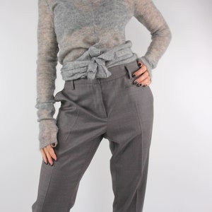 Puede incluir: Un su&eacute;ter gris, transparente, de manga larga, atado a la cintura sobre unos pantalones grises rectos.