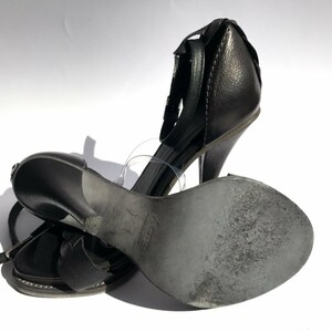 May include: A pair of black leather heeled sandals with ankle straps. The sandals have a closed toe and a high heel.