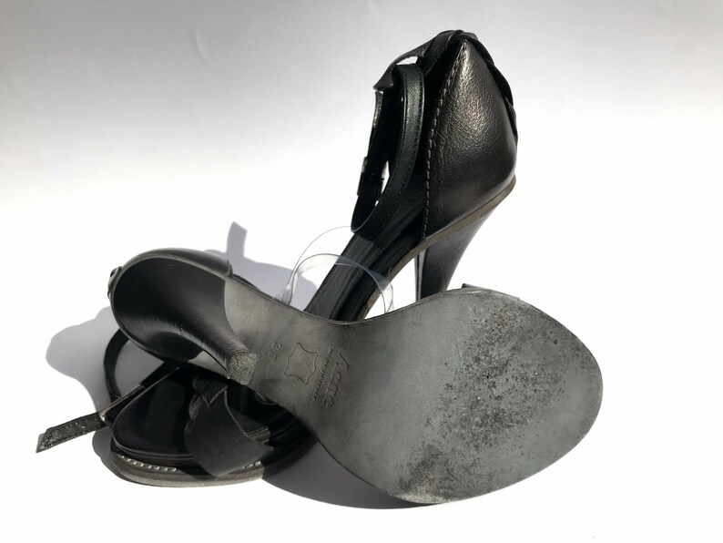 May include: A pair of black leather heeled sandals with ankle straps. The sandals have a closed toe and a high heel.