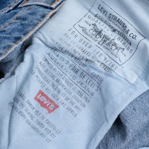 Może przedstawiać: Zbliżenie na niebieską dżinsową kieszeń spodni Levi's z białą metką, na kt&oacute;rej widnieje napis "This is a pair of Levi's Authentic Jeans" oraz "For over 140 years, Levi Strauss & Co. Quality Clothing."