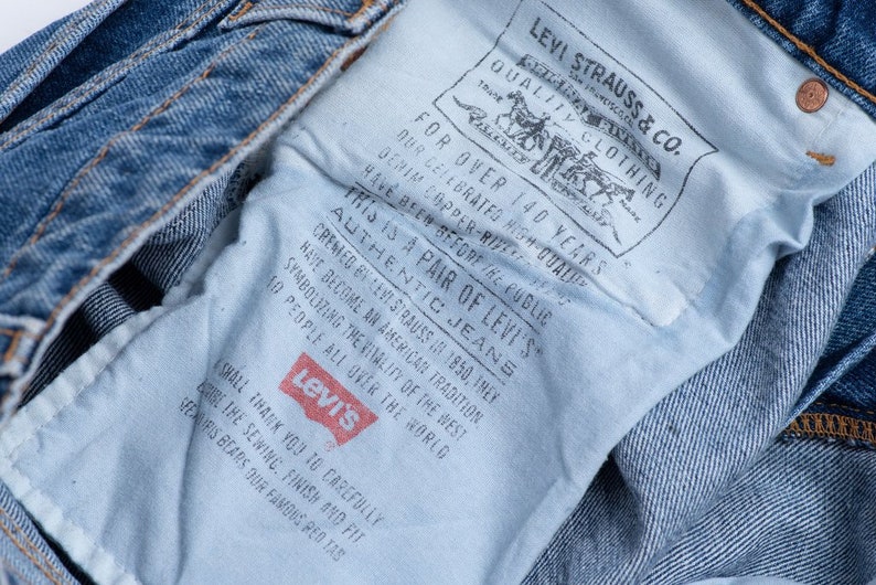 Może przedstawiać: Zbliżenie na niebieską dżinsową kieszeń spodni Levi's z białą metką, na kt&oacute;rej widnieje napis "This is a pair of Levi's Authentic Jeans" oraz "For over 140 years, Levi Strauss & Co. Quality Clothing."