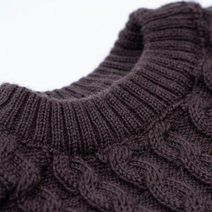 May include: Close-up of a brown cable knit sweater with a ribbed collar.