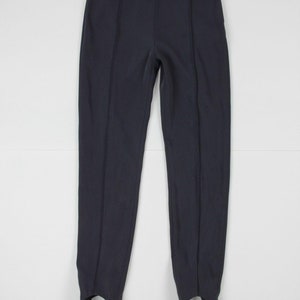 Puede incluir: Pantalones negros con estribos, de cintura alta y costuras verticales. Los pantalones est&aacute;n hechos de una tela oscura y lisa y tienen estribos en los tobillos. Un estilo cl&aacute;sico para ropa deportiva o informal.