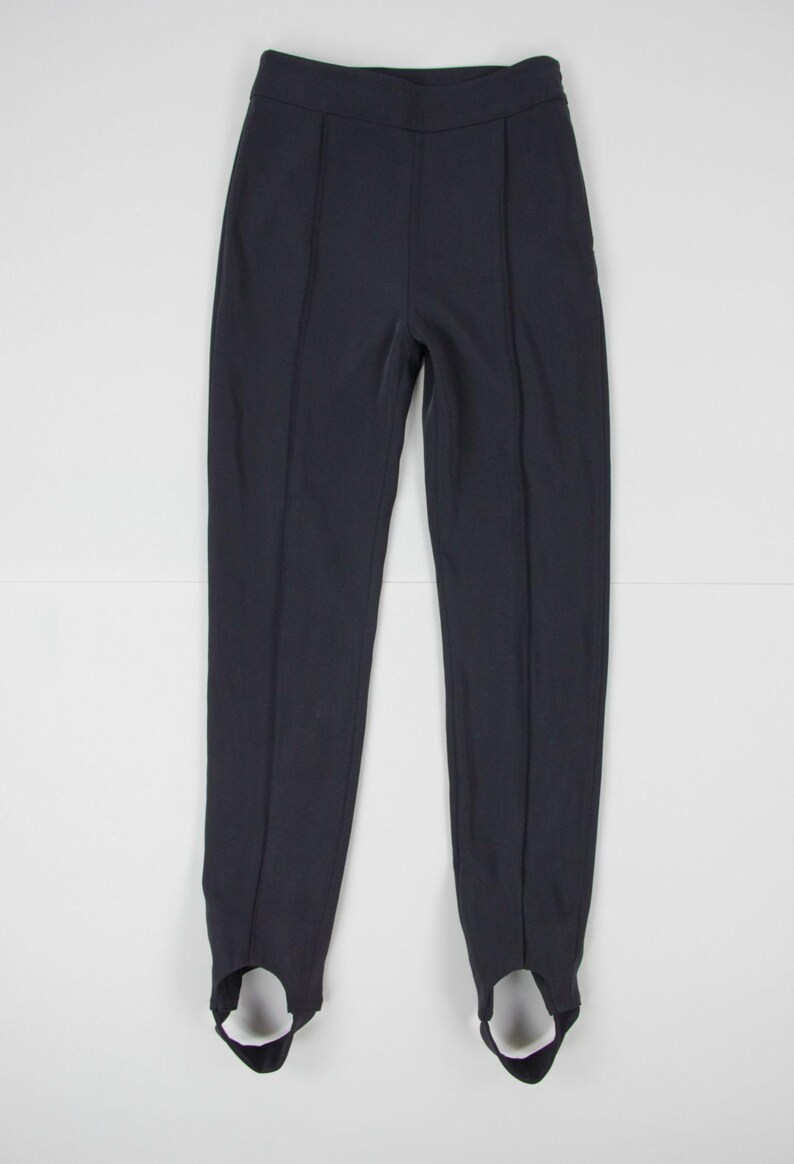 Puede incluir: Pantalones negros con estribos, de cintura alta y costuras verticales. Los pantalones est&aacute;n hechos de una tela oscura y lisa y tienen estribos en los tobillos. Un estilo cl&aacute;sico para ropa deportiva o informal.