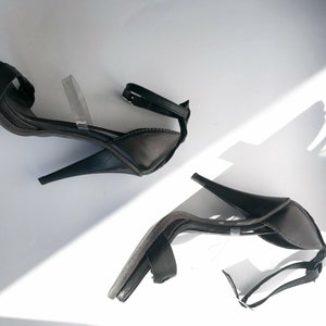 May include: A pair of black heeled sandals with clear straps. The sandals have a closed toe and a high heel.