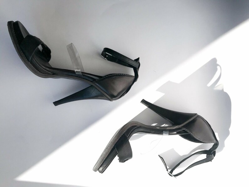 May include: A pair of black heeled sandals with clear straps. The sandals have a closed toe and a high heel.