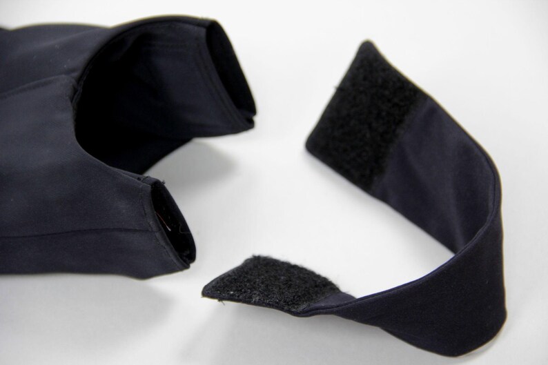 Puede incluir: Una prenda azul marino oscuro con forma curva, con cierre de velcro. La tela parece ser un material liso y mate. El art&iacute;culo se presenta sobre un fondo blanco liso.