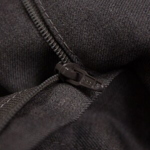 Puede incluir: Primer plano de una cremallera gris oscuro sobre una superficie de tela. La cremallera est&aacute; cerrada y la tela es texturizada.