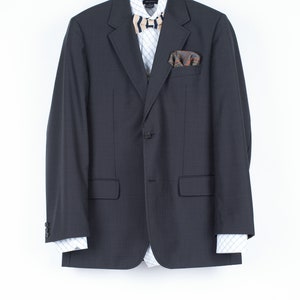 May include: A dark gray blazer with a white and blue patterned shirt, a brown and black bow tie, and a patterned pocket square.