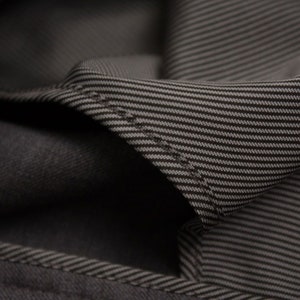 Puede incluir: Primer plano de una tela gris oscura con un sutil patr&oacute;n a rayas. La tela est&aacute; doblada, revelando el reverso del material.