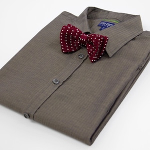 Op de afbeelding: Een bruin overhemd met knopen en een witte en rode geblokte strik. Het overhemd heeft een KENZO-label op de kraag.