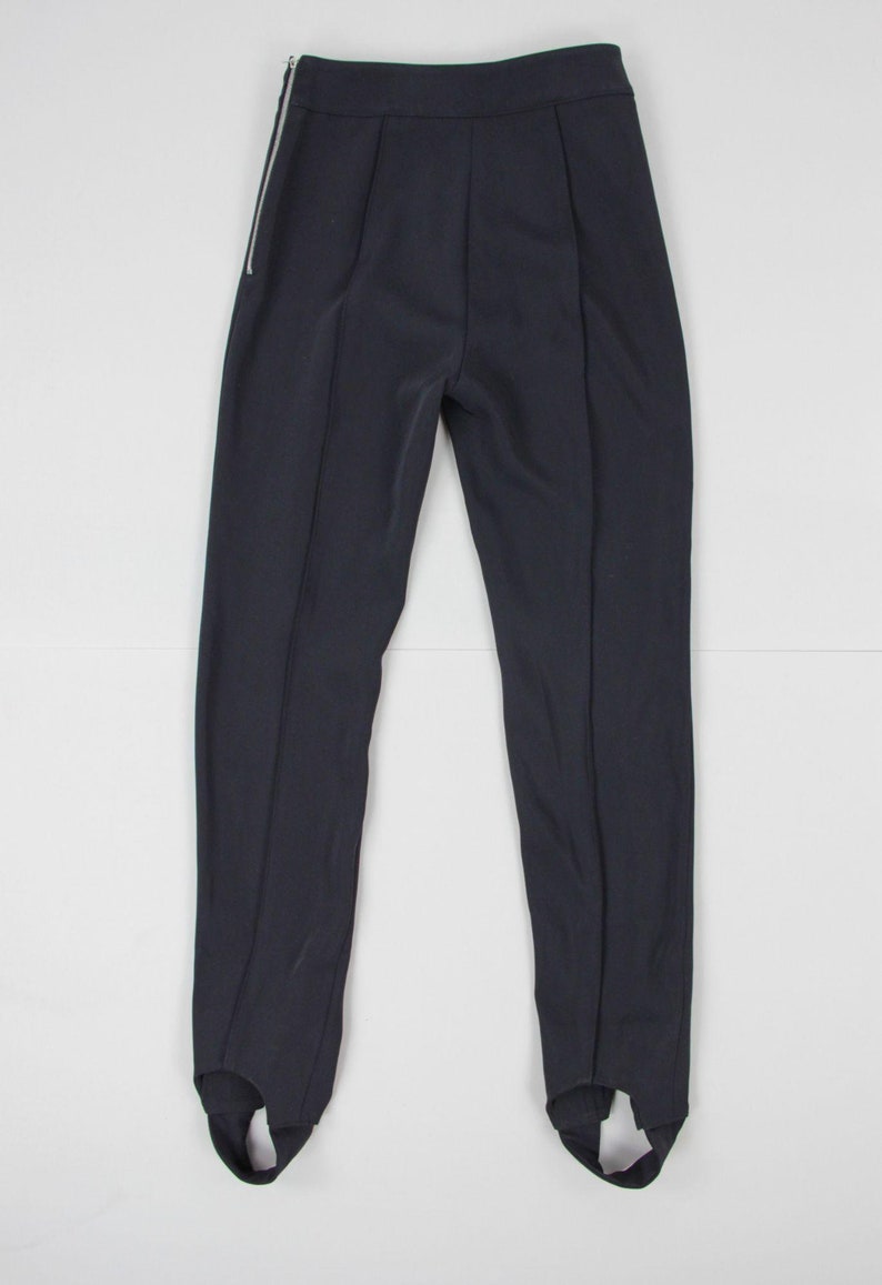 Puede incluir: Pantalones de color azul marino oscuro con estribos y cremallera plateada en el lado izquierdo. Los pantalones tienen cintura alta y costuras verticales en la parte delantera y trasera de las piernas. Los estribos est&aacute;n en la parte inferior.