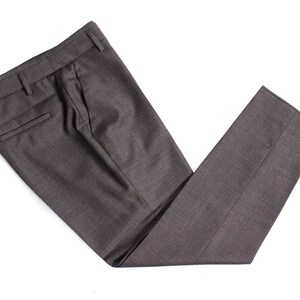 Puede incluir: Un par de pantalones de vestir de color gris oscuro doblados por la mitad. Los pantalones tienen un solo pliegue a cada lado y un bolsillo trasero.