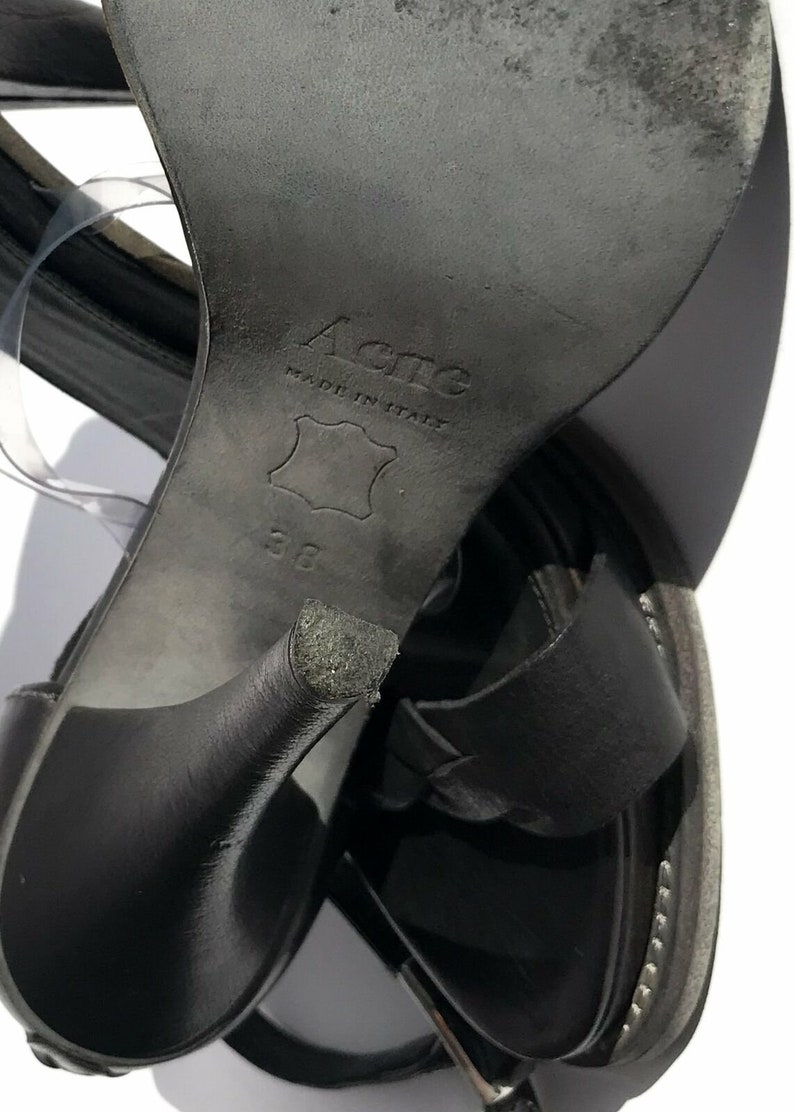 May include: Black leather sandals with a high heel and a buckle closure. The sandals are made in Italy by Acne and are size 38.