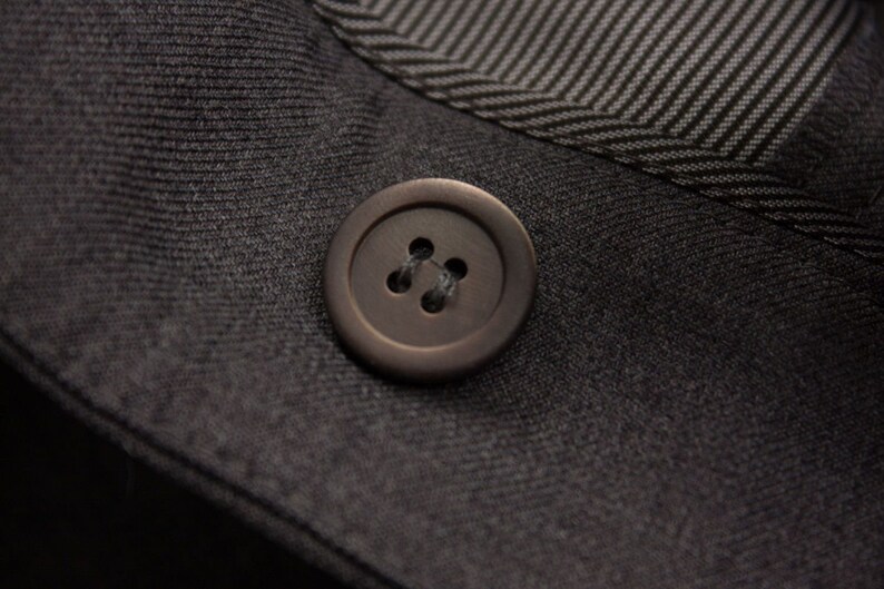 Puede incluir: Primer plano de un bot&oacute;n gris oscuro con cuatro agujeros. El bot&oacute;n est&aacute; cosido a un trozo de tela gris oscuro.