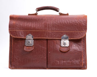 May include: A brown leather briefcase with two metal clasps and a handle. The briefcase has a worn, vintage look.
