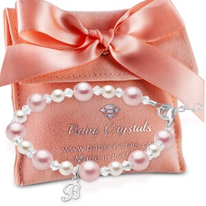 May include: A baby bracelet with pink and white pearls and clear crystals, with a silver charm. The bracelet is displayed on a pink velvet pouch with a matching bow. The pouch has the text "Baby Crystals".