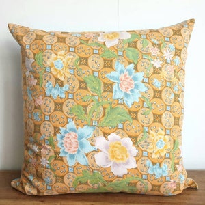 Op de afbeelding: Een geel, blauw en wit kussen met een bloemenpatroon en een geometrisch ontwerp.