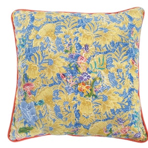 Op de afbeelding: Een geel en blauw patroon kussen met een koraal gekleurde rand. Het kussen heeft een bloemenmotief met ingewikkelde details.