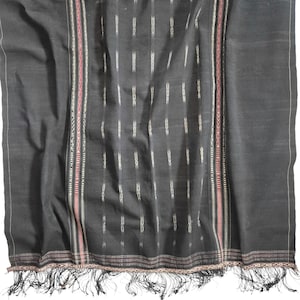 Könnte beinhalten: Ein dunkelgraues Textil mit einem gewebten Muster aus vertikalen weißen Linien und dekorativen Bordüren. Die Bordüren weisen rot-weiße Streifen und komplizierte Designs auf. Der untere Rand hat einen Fransen.