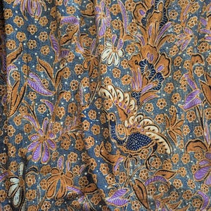 Könnte beinhalten: Ein blauer Stoff mit einem braunen und violetten Blumenmuster. Das Muster zeigt ein sich wiederholendes Design aus Blumen, Blättern und einem Pfau.