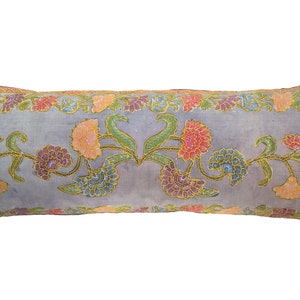 Op de afbeelding: Een lang, rechthoekig kussen met een lichtblauwe achtergrond en een bloemenpatroon in tinten roze, geel, groen en blauw. Het kussen heeft een gouden rand rond de randen.