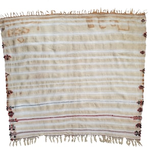 May include: A white woven throw blanket with red and black accents. The blanket has a fringe border and a striped pattern.
