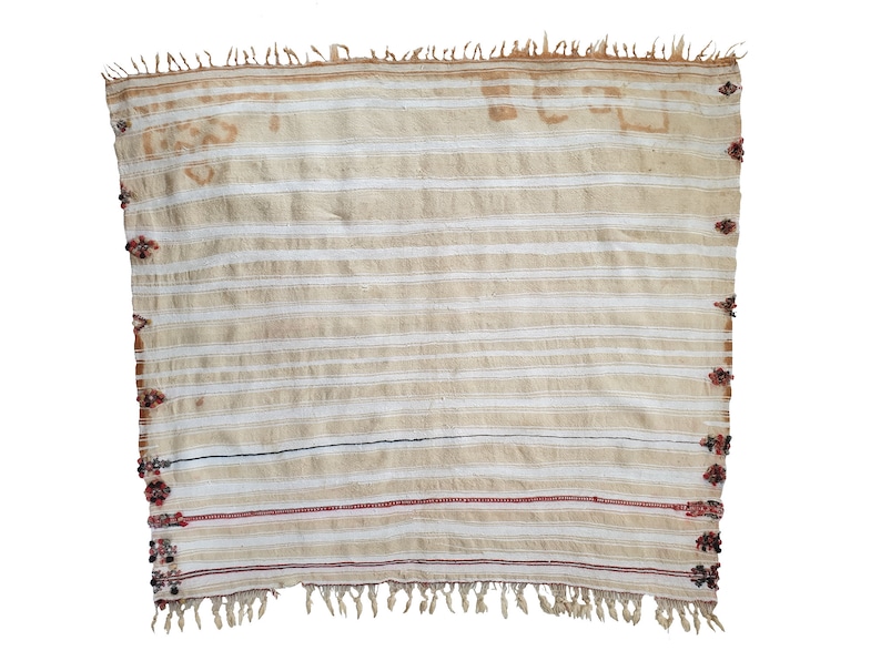 May include: A white woven throw blanket with red and black accents. The blanket has a fringe border and a striped pattern.