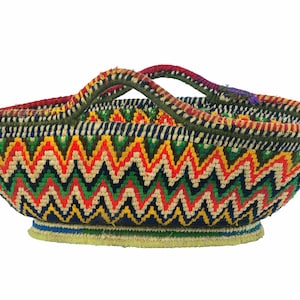 May include: A colourful, hand-woven basket with a zigzag pattern in red, yellow, green, and blue. The basket has a rounded shape with a sturdy handle and a flat base. The rim and handle are trimmed with green and red.