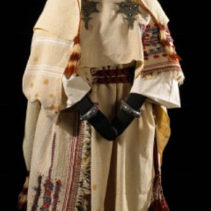 May include: A white robe with red and blue embroidery, a silver headpiece with red jewels, and a red tassel. The robe is worn over a white tunic with silver embellishments.