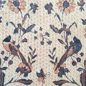 May include: A beige fabric with a repeating pattern of brown and blue flowers, leaves, and birds. The birds are perched on branches and have long tails.