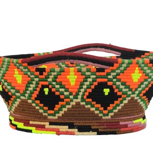 Peut inclure: Un panier tissé avec un motif géométrique orange, noir, vert et marron. Le panier a deux anses et un design coloré. Le panier mesure environ 30 cm de large et 20 cm de haut.