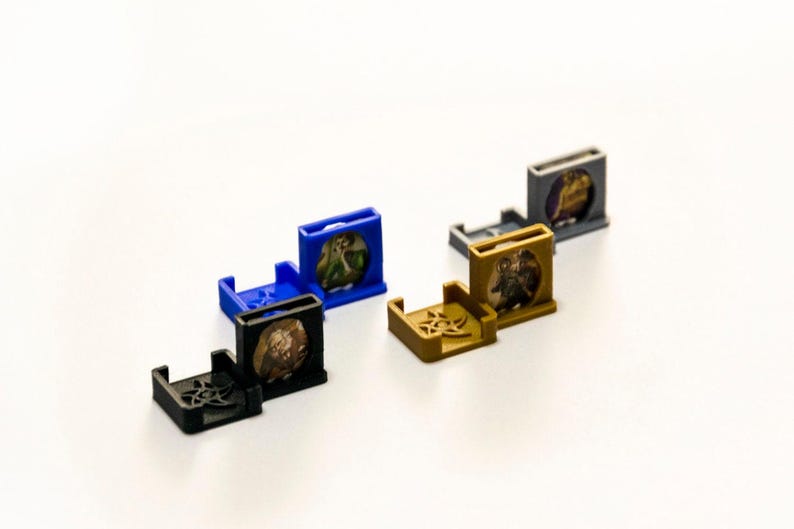 May include: Six small, colourful plastic stands with different designs. Each stand has a small circular space to hold a miniature figure or game piece. The stands are blue, black, grey, and gold.