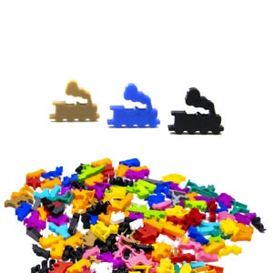 May include: A collection of colorful plastic toy pieces, including three train-shaped pieces in tan, blue, and black. The pieces are scattered on a white background, with a variety of other shapes and colors in the foreground.