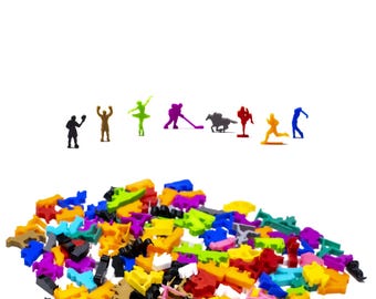 Könnte beinhalten: Eine bunte Auswahl an kleinen Plastikfiguren, darunter verschiedene Sportfiguren, eine Ballerina und eine Person mit einem Mikrofon. Die Figuren sind auf einer weißen Oberfläche verstreut.