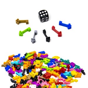 May include: A black six-sided die with white dots, along with a variety of colourful plastic keys. The keys are in different shapes and sizes, and some have a small hole in the centre. The keys are scattered on a white surface.