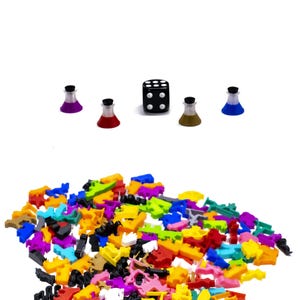 May include: A black six-sided die with white dots, surrounded by five colourful plastic beakers. A large pile of colourful plastic game pieces are in the foreground.