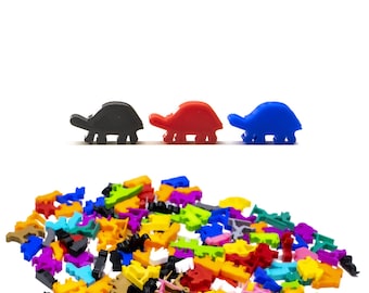 May include: A collection of colorful, miniature plastic turtle figurines in various colors, including black, red, and blue. The turtles are arranged in a pile, with three turtles lined up at the top. These small toys are likely for a board game or craft project.