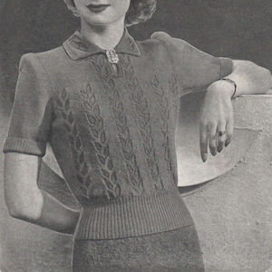 May include: A black and white photograph of a woman wearing a knitted jumper with a leaf pattern. The jumper has a collared neckline and short sleeves. The woman is wearing a brooch on her collar.