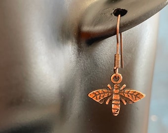 May include: A pair of copper-toned dangle earrings featuring a detailed bee charm. The earrings have a simple wire hook closure.