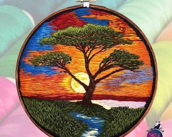 May include: Hand-stitched embroidery hoop art featuring a sunset landscape with a lone tree, a river, and a bright orange sun. The background is a gradient of orange, red, and blue.