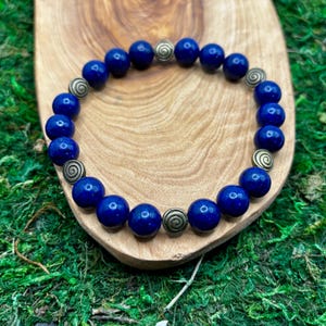 May include: A blue gemstone bracelet with gold-toned metal beads. The bracelet is made of round beads with a smooth, polished finish.