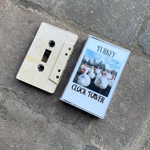 May include: A white cassette tape with the title "TURKEY CLOCK TOWER" printed on the front. The cassette tape has a picture of a group of turkeys on the front.