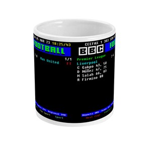 Op de afbeelding: Witte keramische mok met een zwarte achtergrond met een retro voetbalscore-afbeelding. De afbeelding bevat het BBC-logo, teamscores en spelersnamen. De mok heeft een gebogen handvat en een glanzende afwerking.