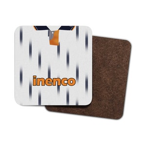 May include: Square coaster with a white background and a pattern of vertical dark blue lines. The coaster features a design resembling a jersey, with the word "inenco" in orange. A second coaster with a brown cork backing is visible.
