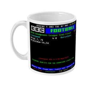Puede incluir: Taza de cerámica blanca con un panel negro que muestra el texto BBC Football y un marcador de partido. El texto incluye el marcador de la semifinal de la Liga de Campeones de la UEFA: Liverpool 4-0 Barcelona. La taza tiene un asa curva.