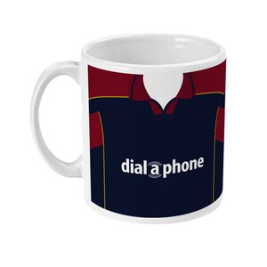 Könnte beinhalten: Weiße Keramik-Tasse mit einem marineblauen und weinroten Trikot-Design und dem Text "dial a phone". Die Tasse hat einen weißen Henkel und Innenraum, ideal für Kaffee, Tee oder jedes Getränk.