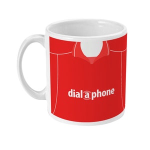 Könnte beinhalten: Weiße Keramik-Tasse mit rotem Design, das einem Trikot ähnelt. Die Tasse trägt den weißen Schriftzug "dial a phone" und einen weißen Henkel. Das Design beinhaltet ein weißes Kragendetail.